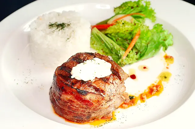 Bacon-wrapped beef fillet with herb butter, rice and salad