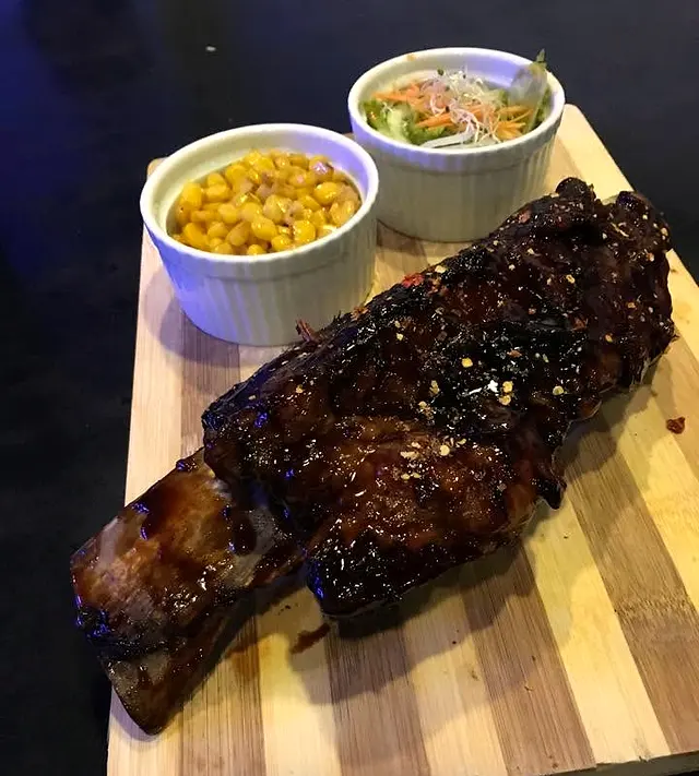 Glazed rack of ribs with corn and coleslaw on a wooden board