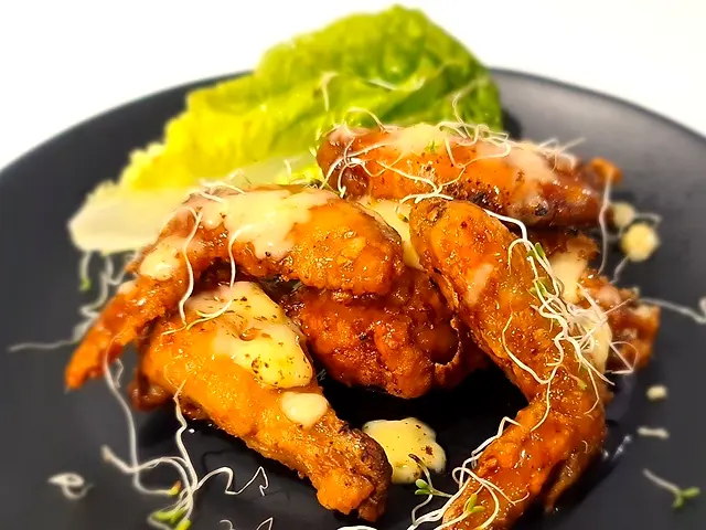 Glazed chicken wings with cheese sauce and lettuce on a dark plate